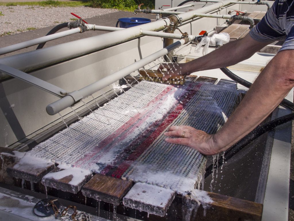 Henkilö pesee ulkona mattoa