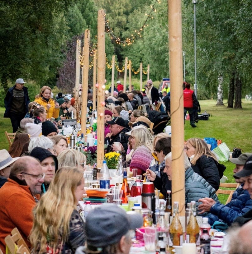 Ihmisiä illallistamassa pitkän pöydän ääressä ulkoilmassa.