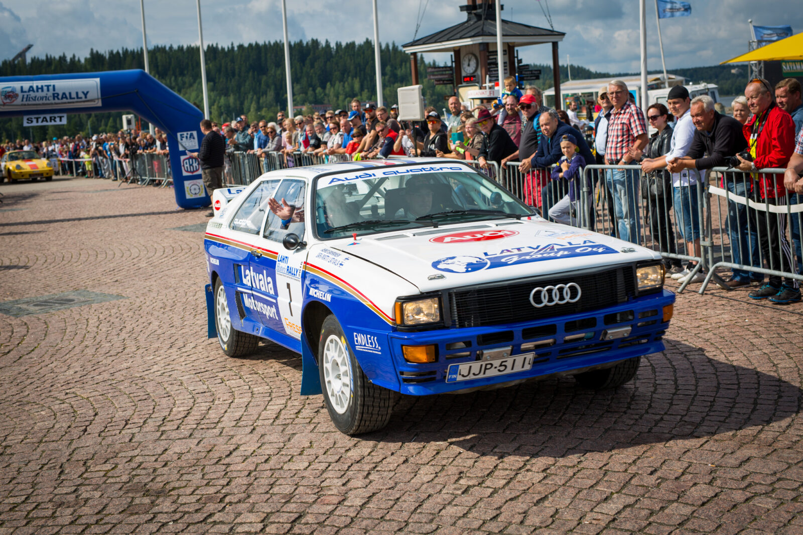 Valkosininen ralliauto, yleisöä auton taustalla.