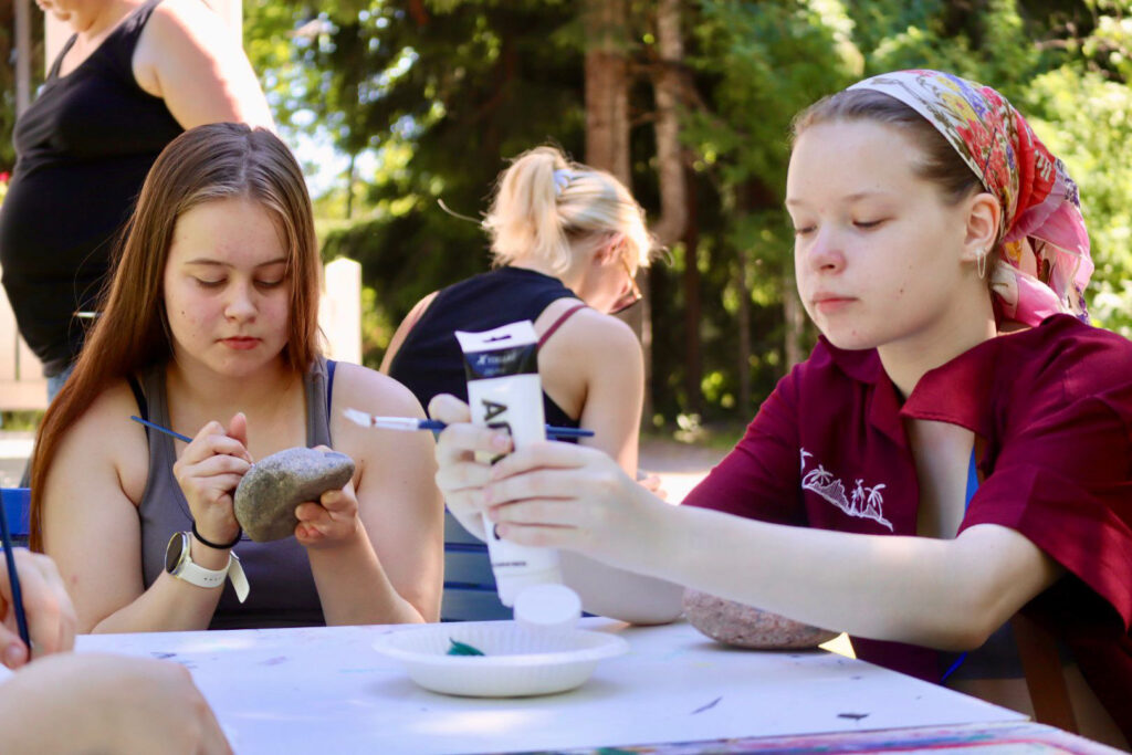 tytöt malaa kiviä ulkona pöydän ääressä
