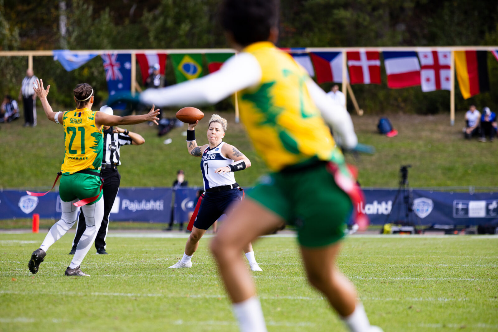 Valkoinen-sinipaitainen henkilö heittää amerikkalaista jalkapalloa, keltapainen henkilö yrittää estää heittoa.