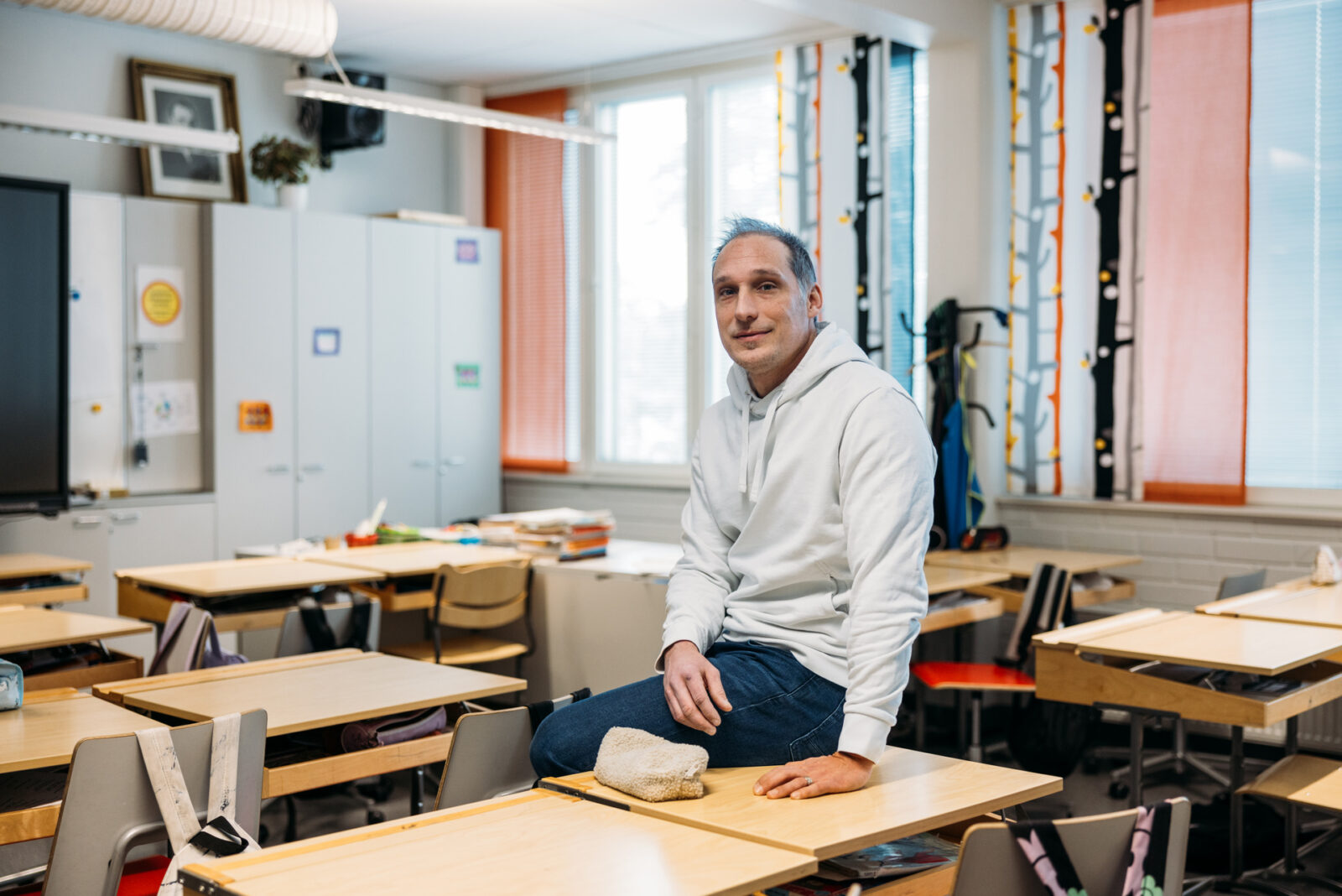 Esa Liukkonen istuu pulpetin päällä keskellä luokkaa ja katsoo kameraan