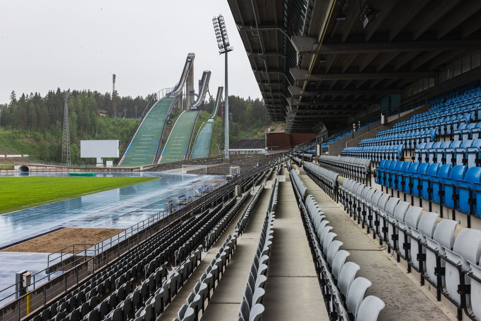 Kuvassa Lahden urheilukeskuksen katsomo ja taustalla hyppyrimäet.