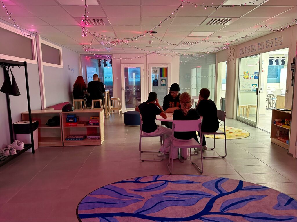 Aulassa tunnelmavaloissa nuoret pelaamassa lautapelejä kahden pöydän ääressä. Edessä sininen matto lehti koristeilla.