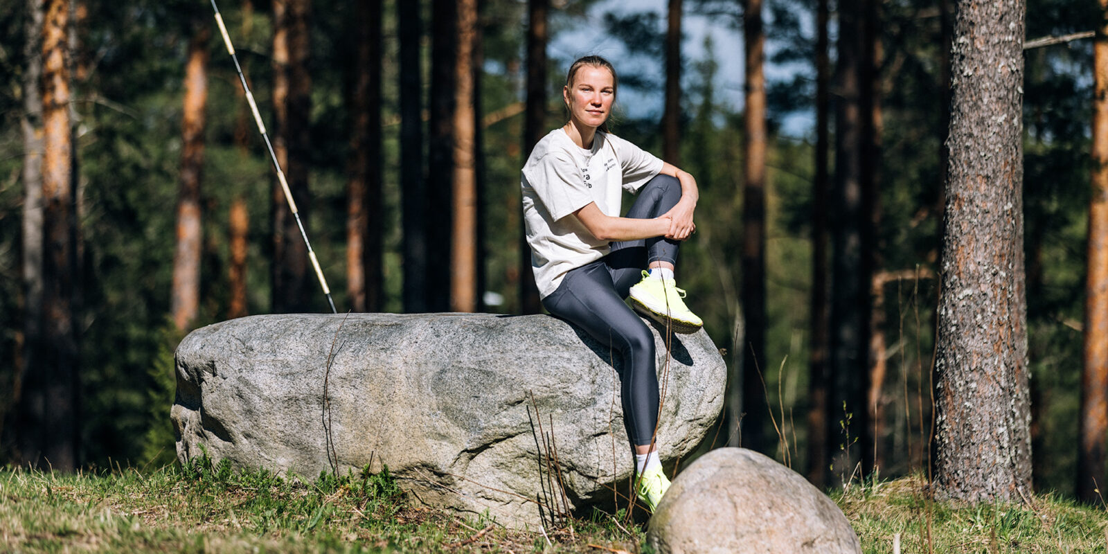 Kestävyysjuoksija Ilona Mononen istuu auringonpaisteessa metsässä kivellä.