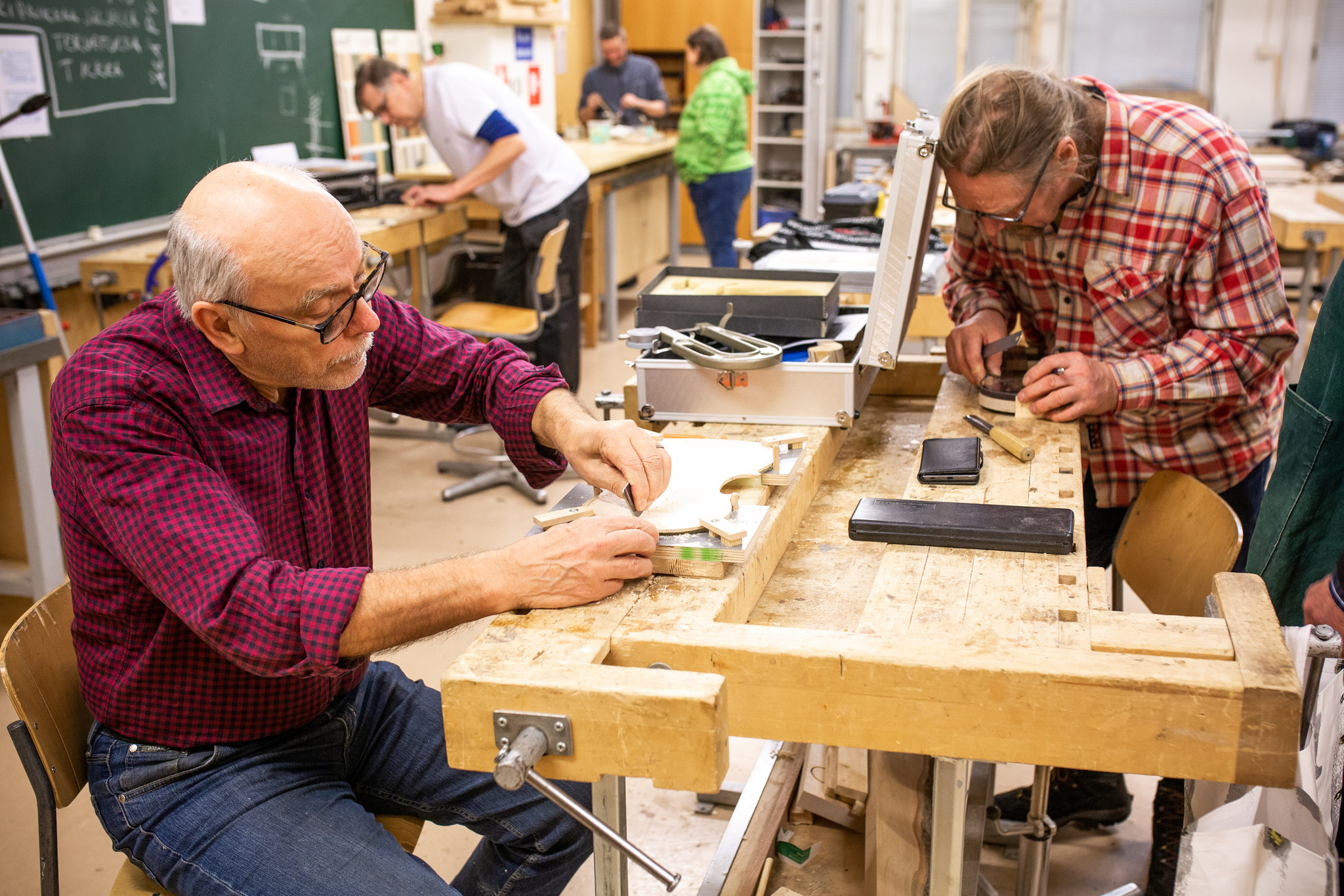 Kaksi miestä työskentelee puutyöpöydän äärellä käsitöitä.